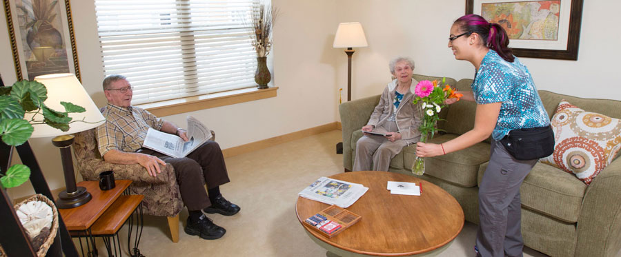 elderly couple in an Attic Angel Apartments living room receiving flowers from a younger female