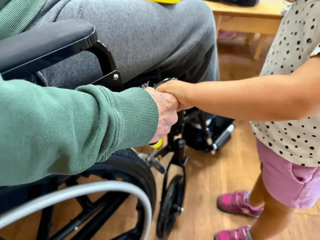 young girl holding elderly person's hand in wheelchair
