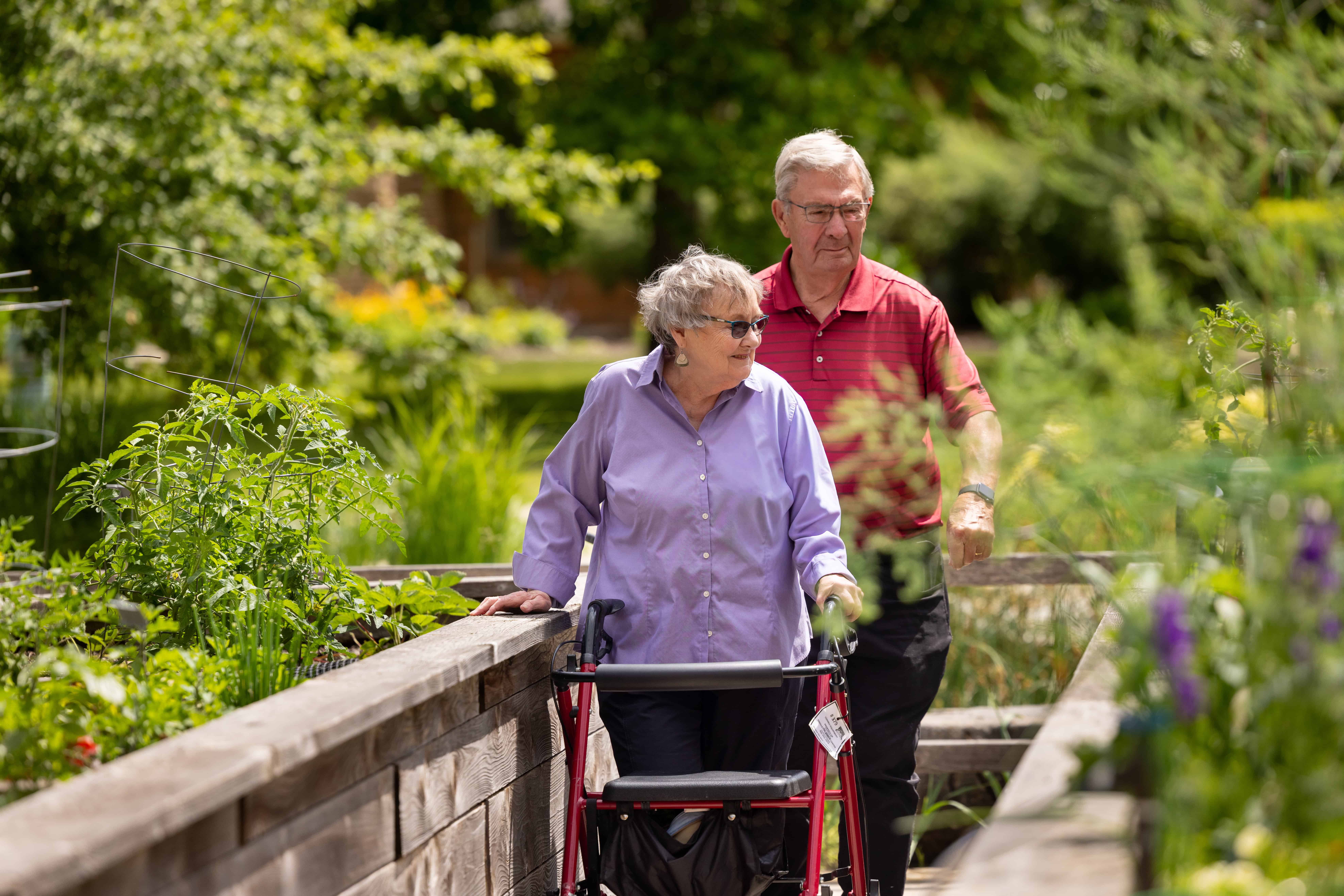 older man and woman with walker walking in garden